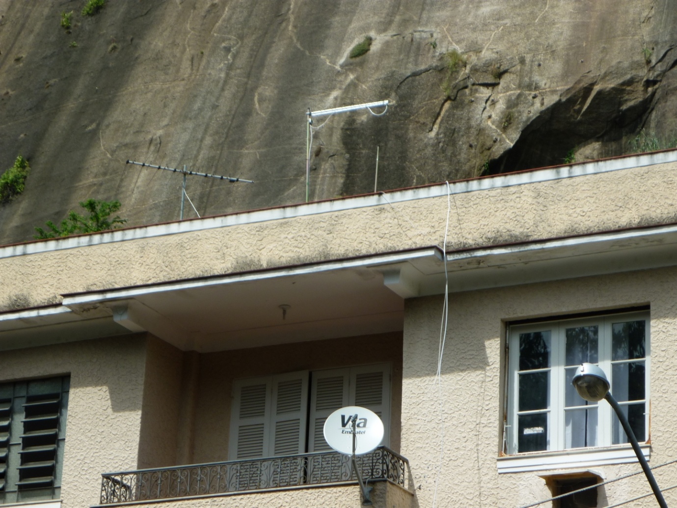 Uma antena UHF solitária, em uso para DTV, próxima de outra, VHF, abandonada. No apartamento de baixo, a situação de quem vive em locais sem sinal analógico de televisão, dentro da área urbana da cidade.